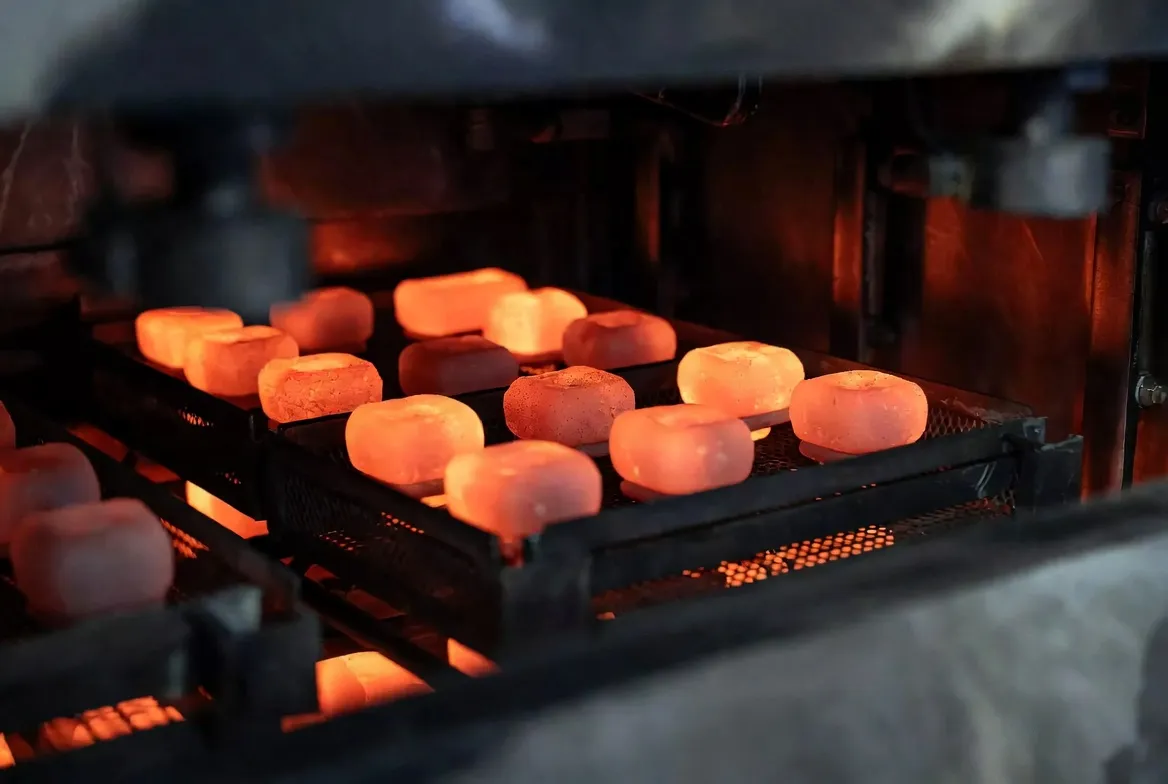 Multiple CNC steel industrial parts glowing orange-red while being batch heated on trays inside an industrial heat treatment furnace.