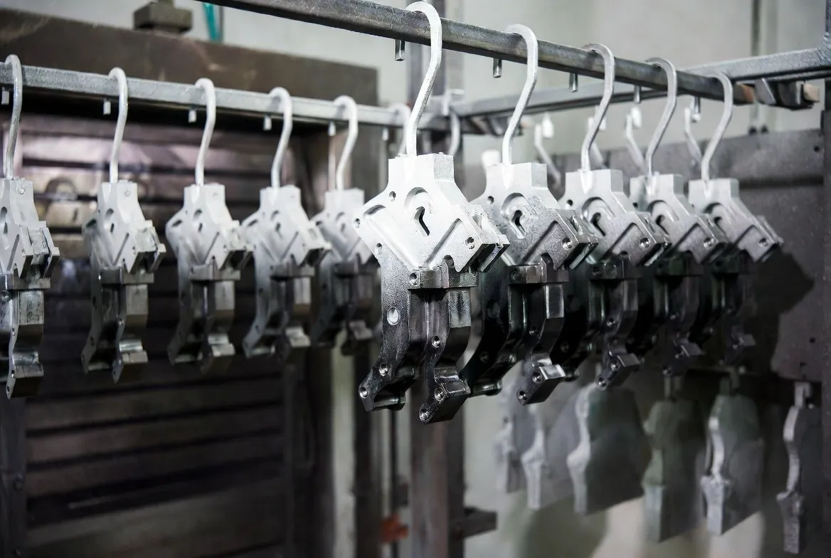 Multiple CNC steel industrial parts hanging on racks covered with dry powder coating, ready to enter the curing oven.