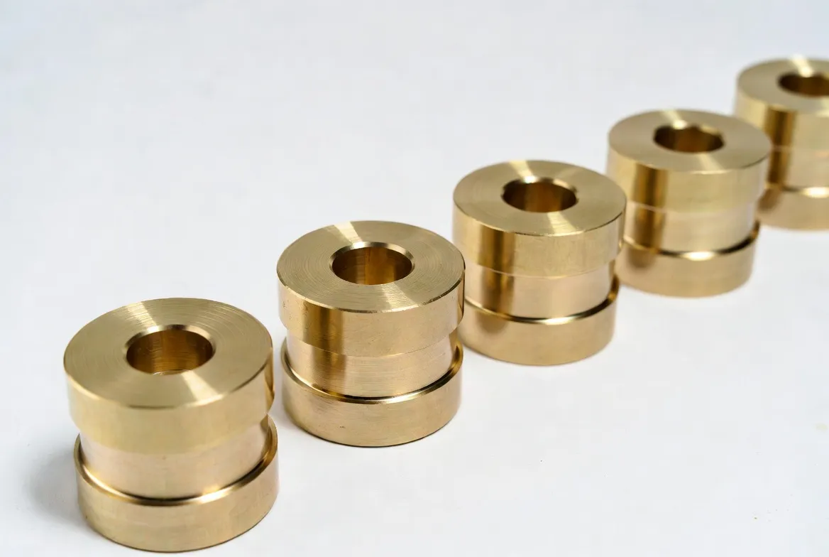 Multiple identical brass CNC precision bushings and collars arranged neatly in a row on a white background.