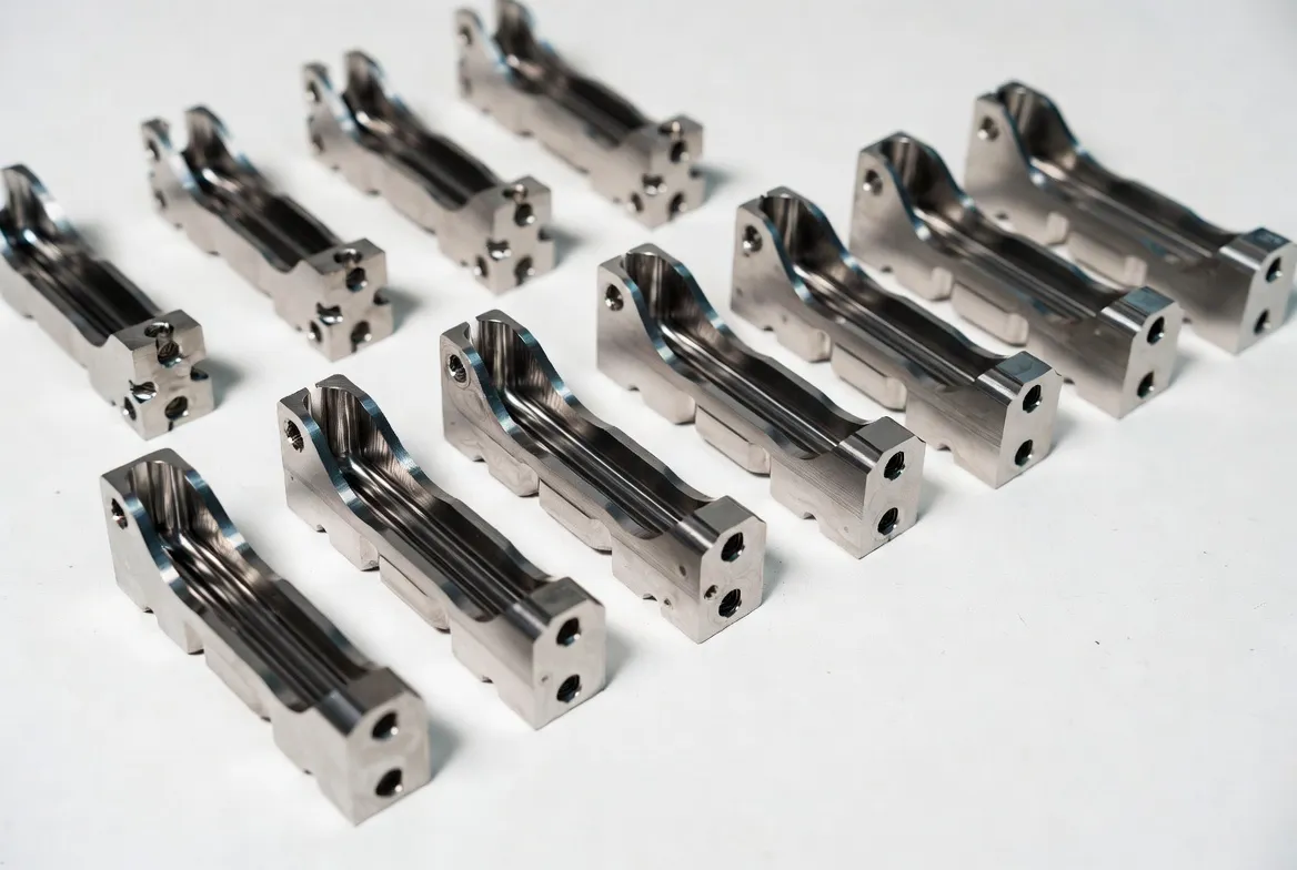 Multiple identical titanium alloy CNC precision components arranged neatly in a row on a white background.