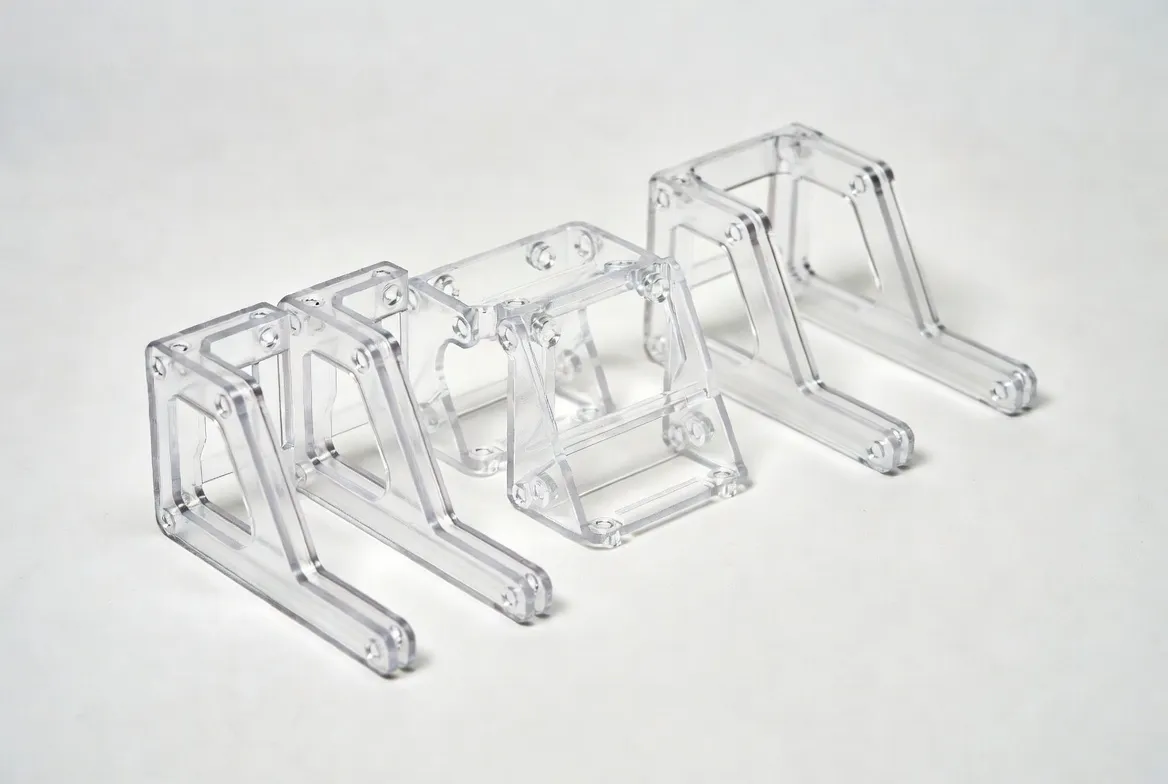 Multiple identical clear PC polycarbonate CNC industrial structural brackets arranged neatly in a row on a white background.